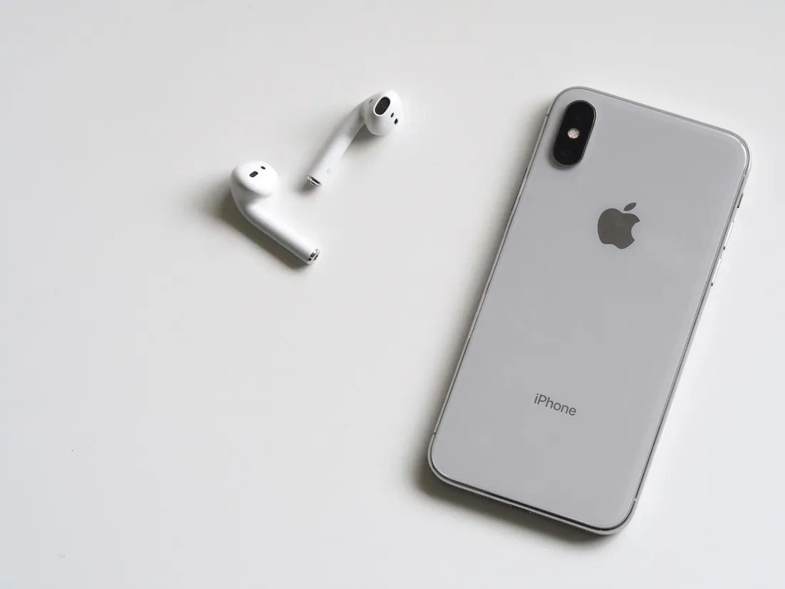 Silver iPhone and white wireless earbuds on a white surface