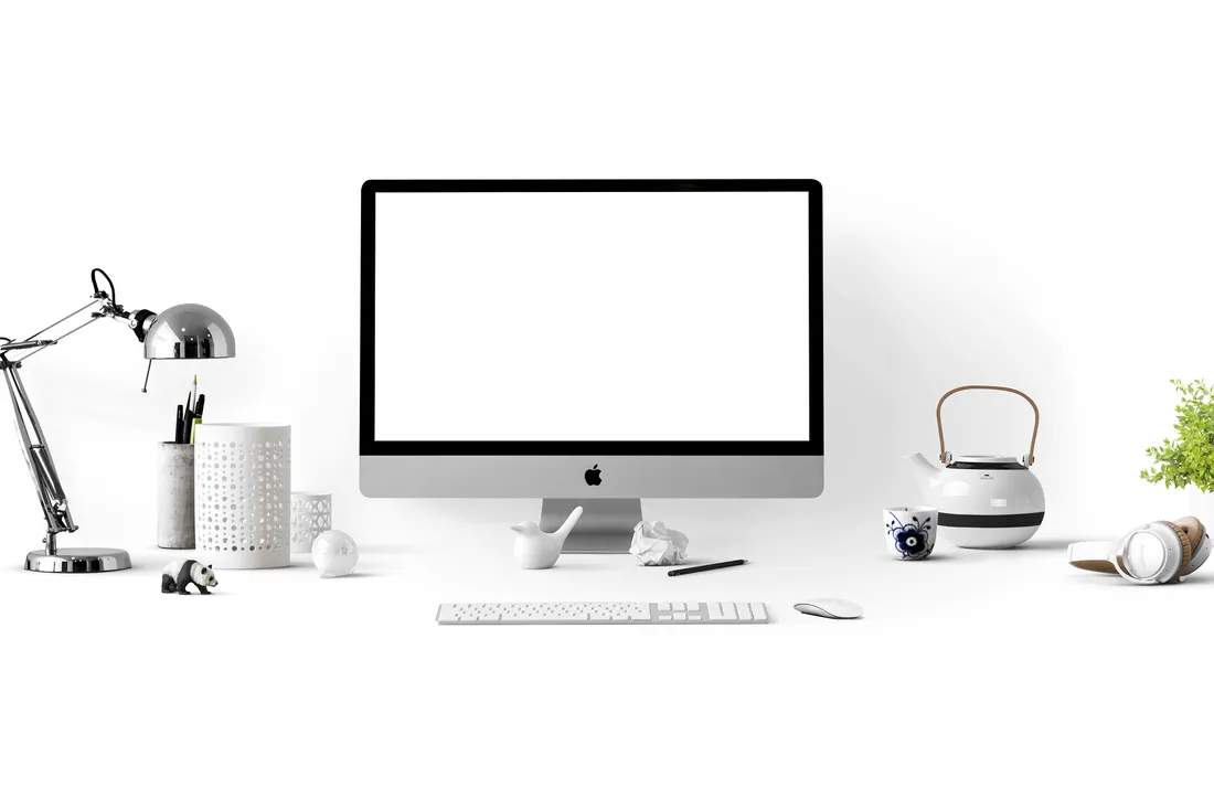 A clean white desk with an iMac computer, keyboard, mouse, desk lamp, and small decorative items