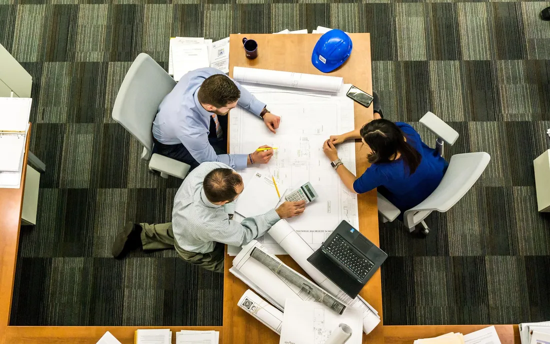 Team of professionals gathered around a table reviewing architectural blueprints in an office meeting