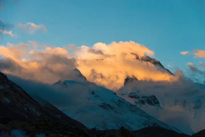 Snow-capped Himalayan peak with golden clouds at sunrise or sunset and prayer flags below