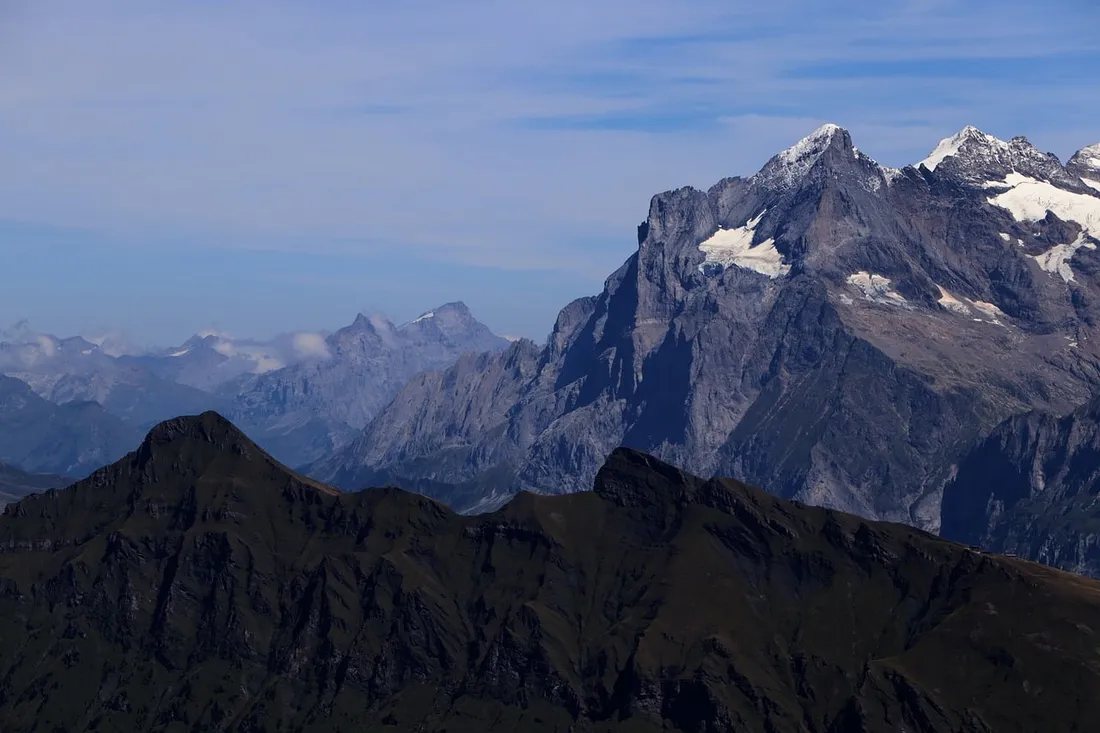 Snow-capped Swiss Alps rising above dark foreground ridges beneath a blue sky.