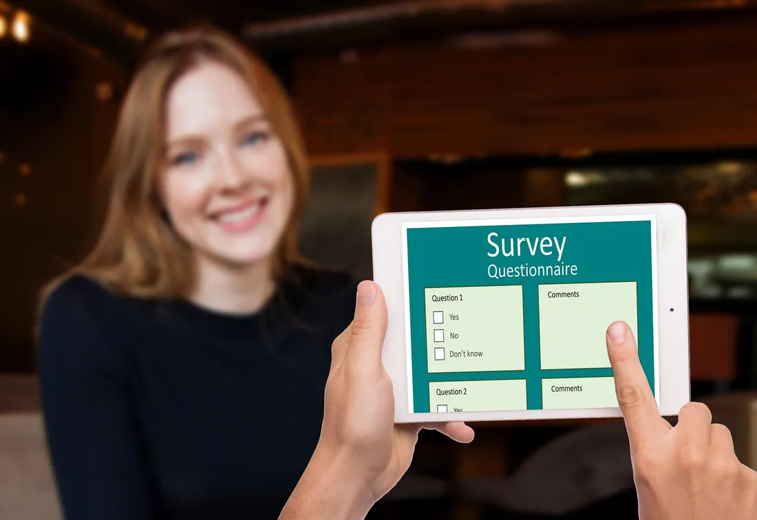 A woman holding a tablet displaying a survey questionnaire with yes, no, and don't know checkboxes