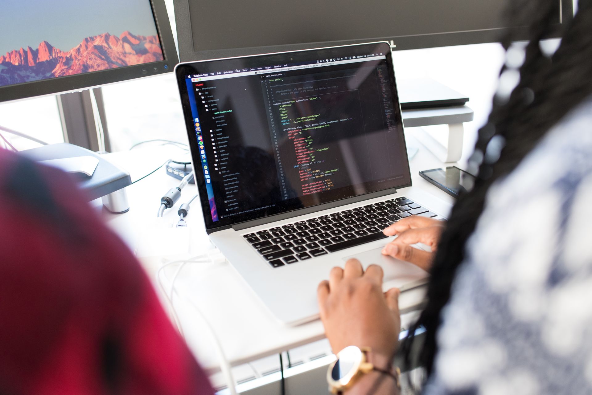 Developer typing on a laptop with JavaScript code visible in an editor