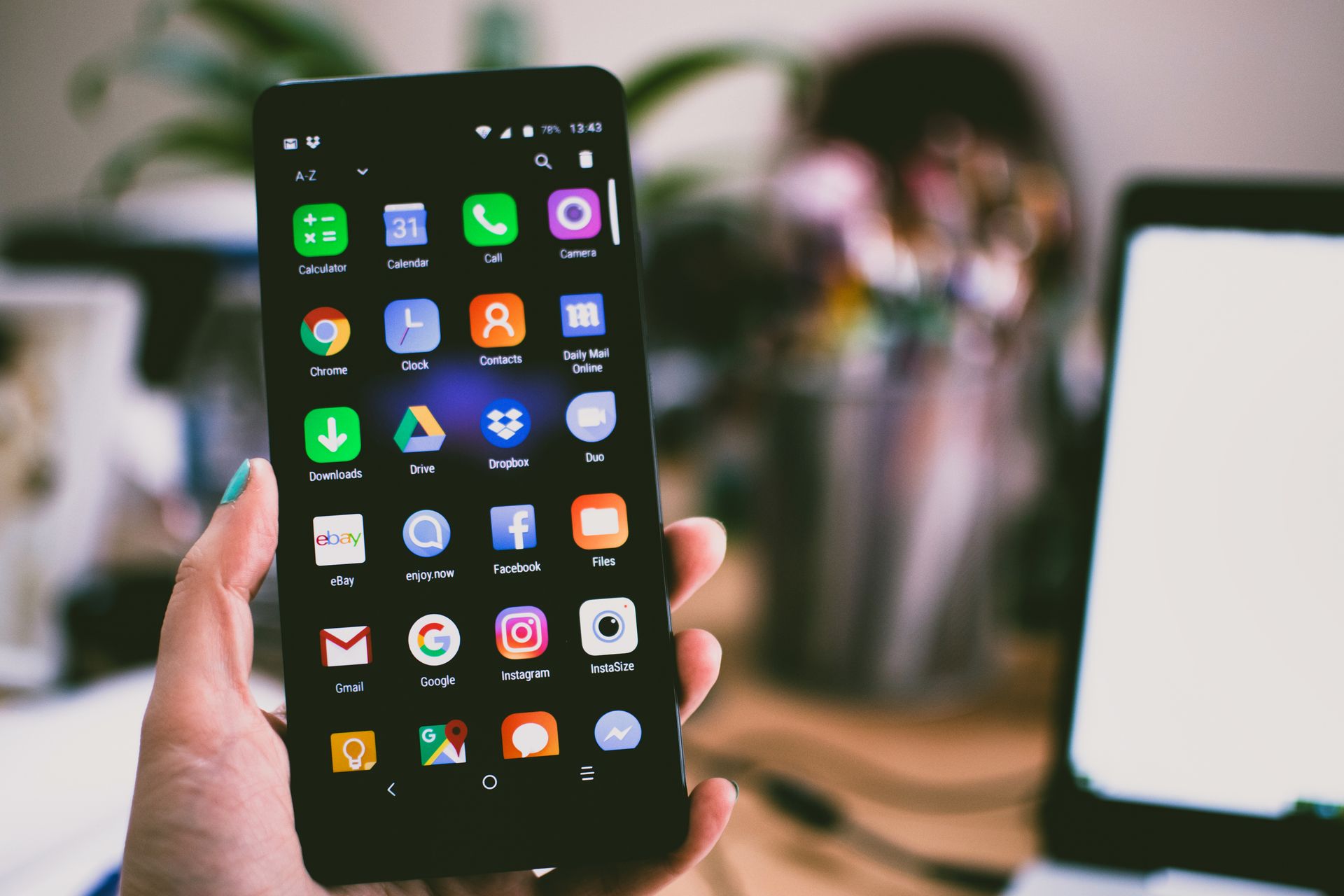 Hand holding an Android smartphone showing a grid of app icons