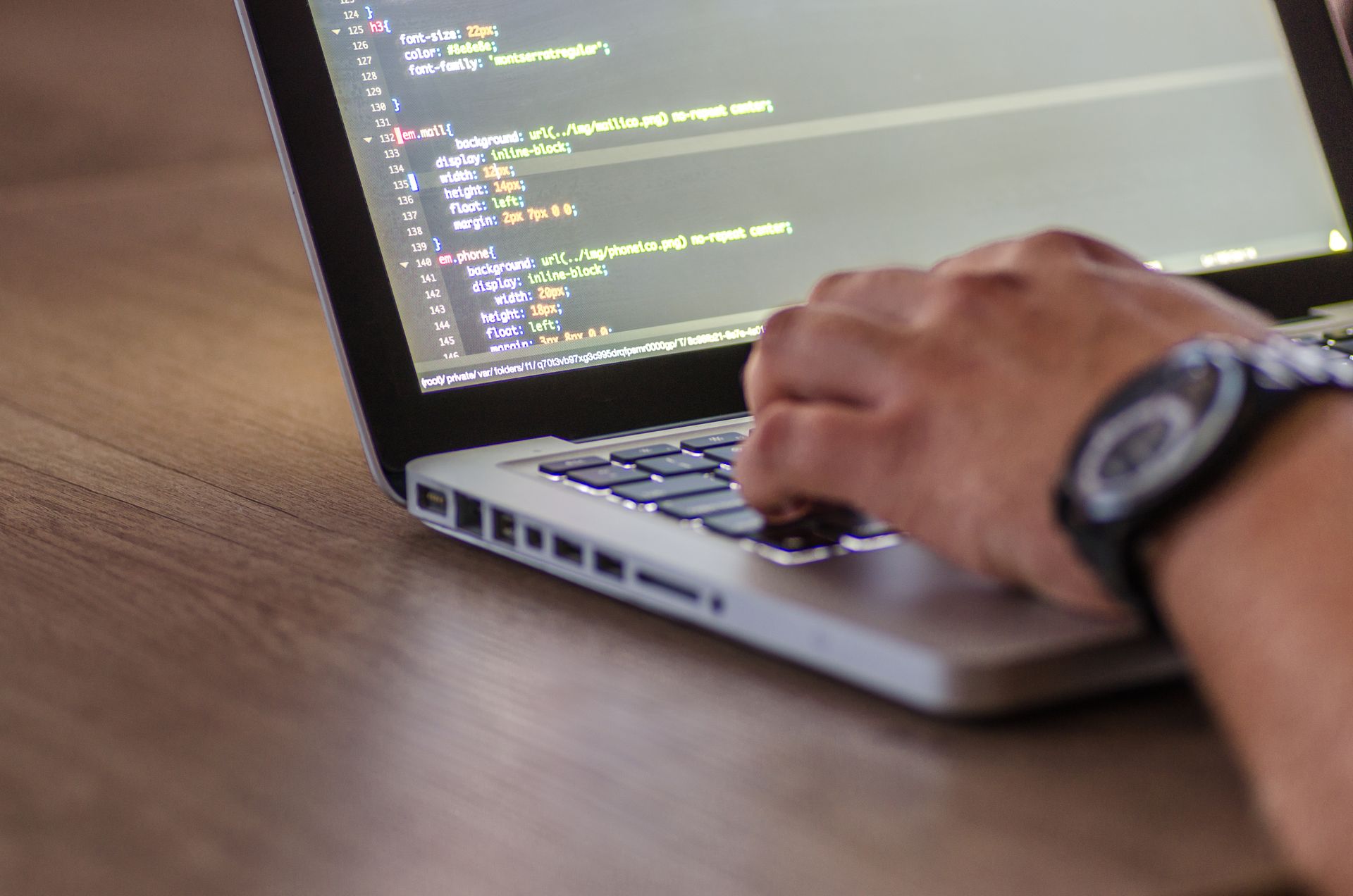 Hands typing on a silver laptop showing CSS code on the screen