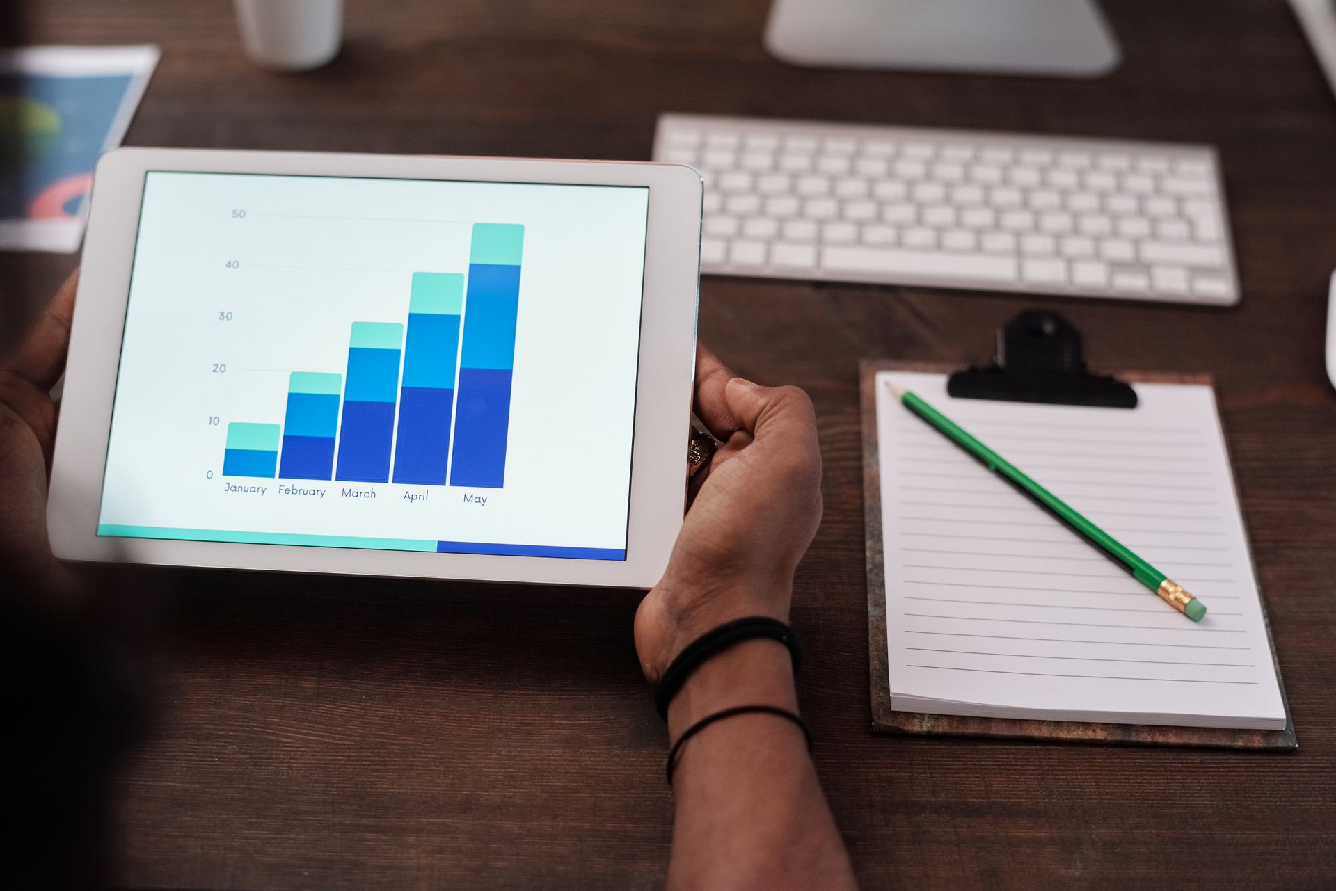 Hands holding a tablet displaying a bar chart on a wooden desk