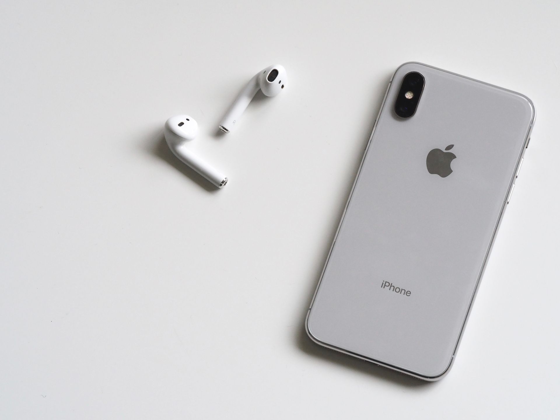Silver iPhone and white wireless earbuds on a white surface
