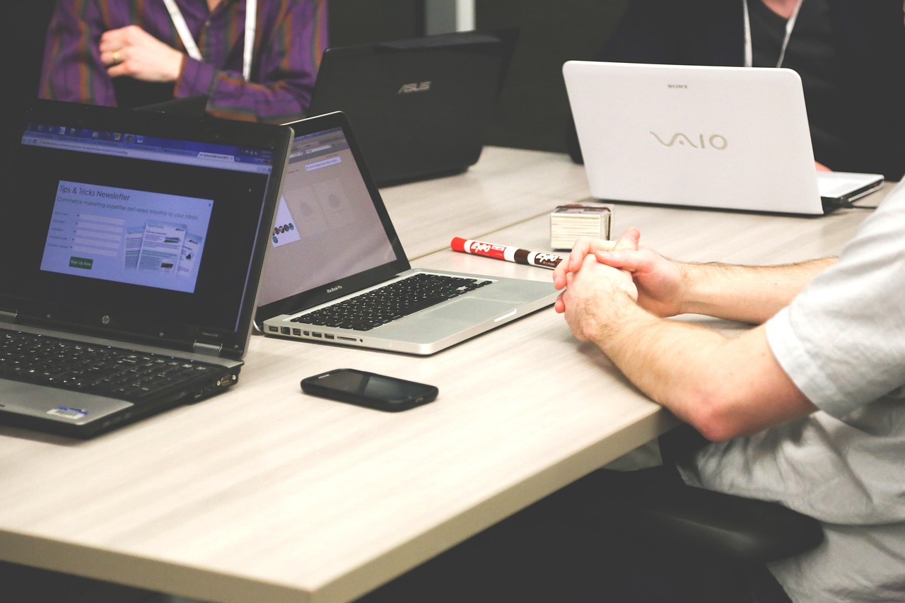 Several open laptops on a light wooden table during a team work session, with a phone and marker nearby