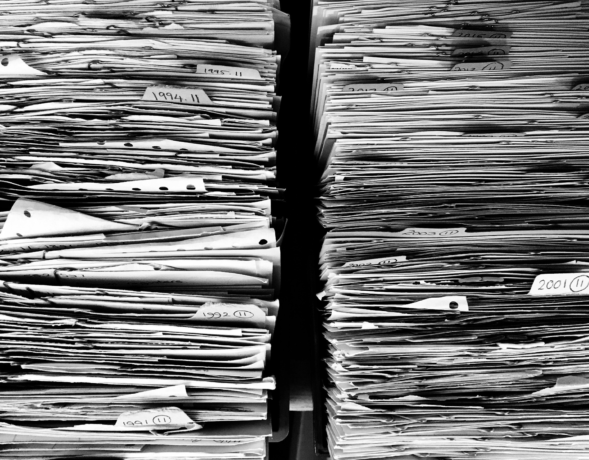 Black and white photo of stacked paper files and folders in an office archive