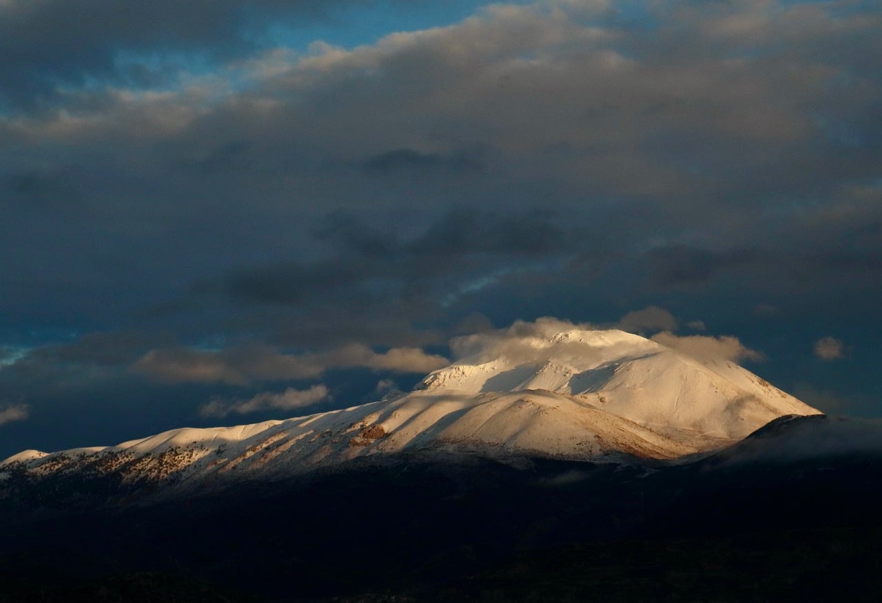 Snow-covered mountain peak glowing beneath dark storm clouds.