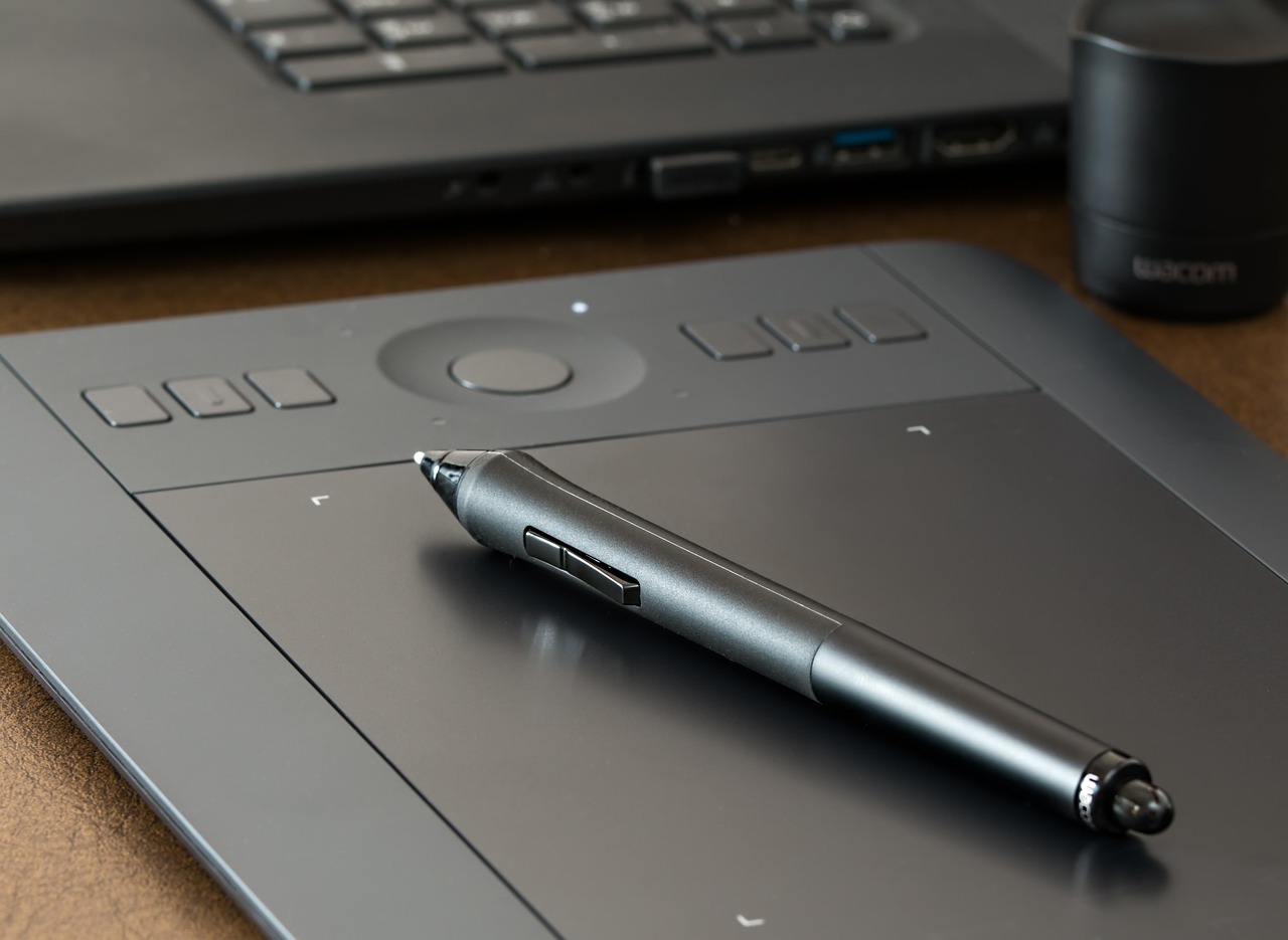 Close-up of a graphics tablet and stylus pen on a desk next to an open laptop
