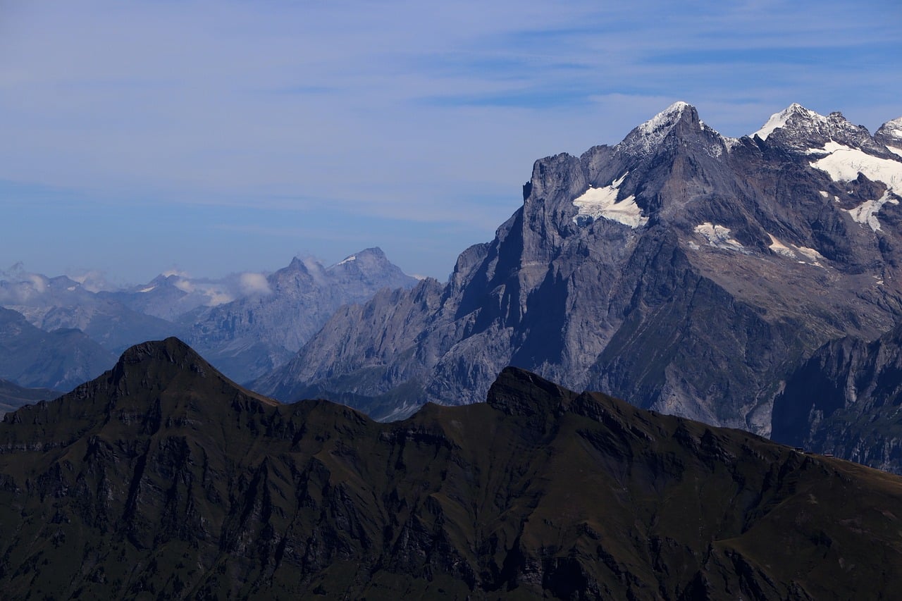 Snow-capped Swiss Alps rising above dark foreground ridges beneath a blue sky.