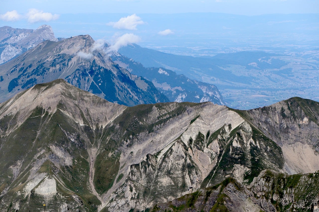 A wide view of rugged Alpine mountain ridges under a blue sky with scattered clouds.