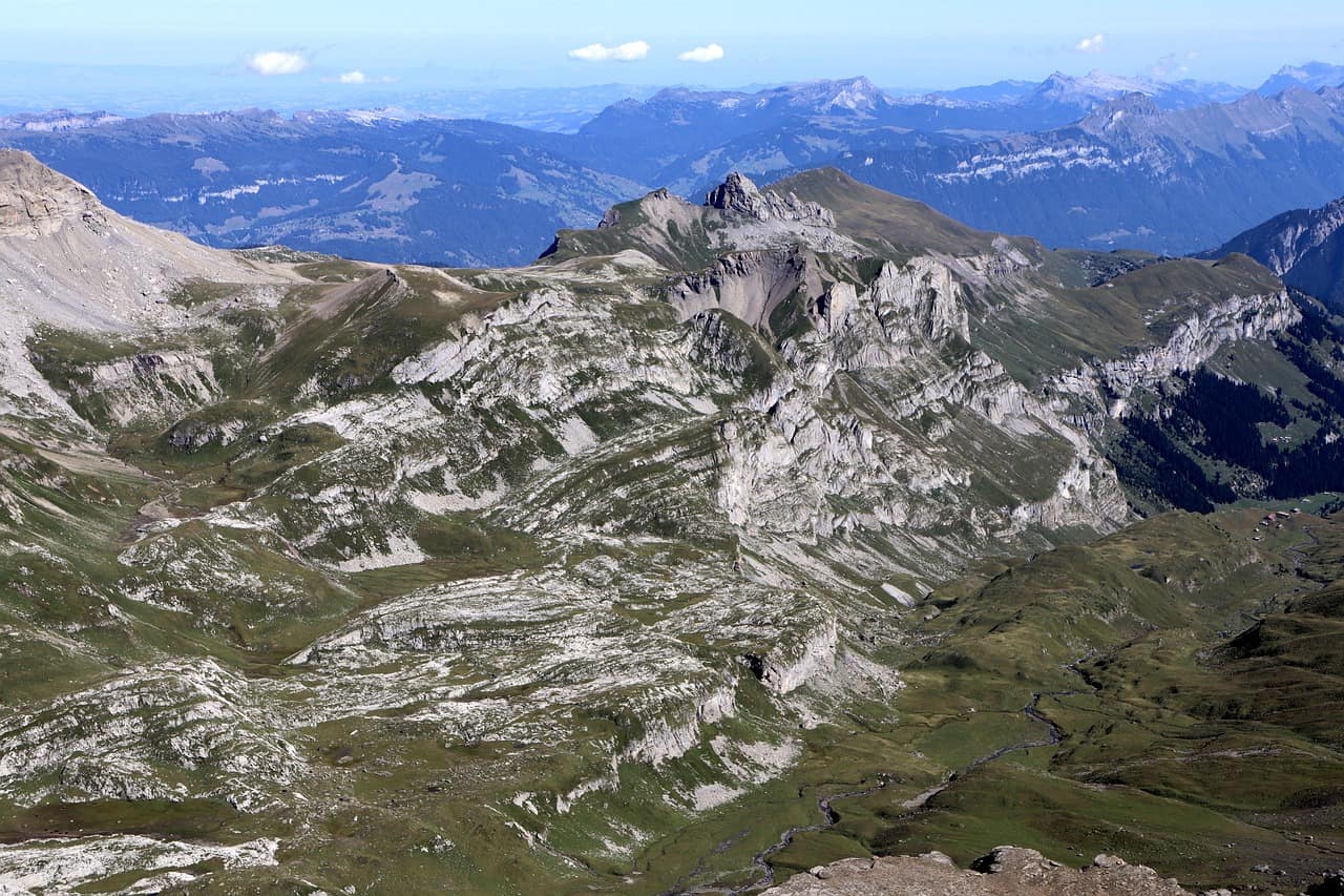Aerial view of a rocky green Alpine mountain range with a hazy blue horizon