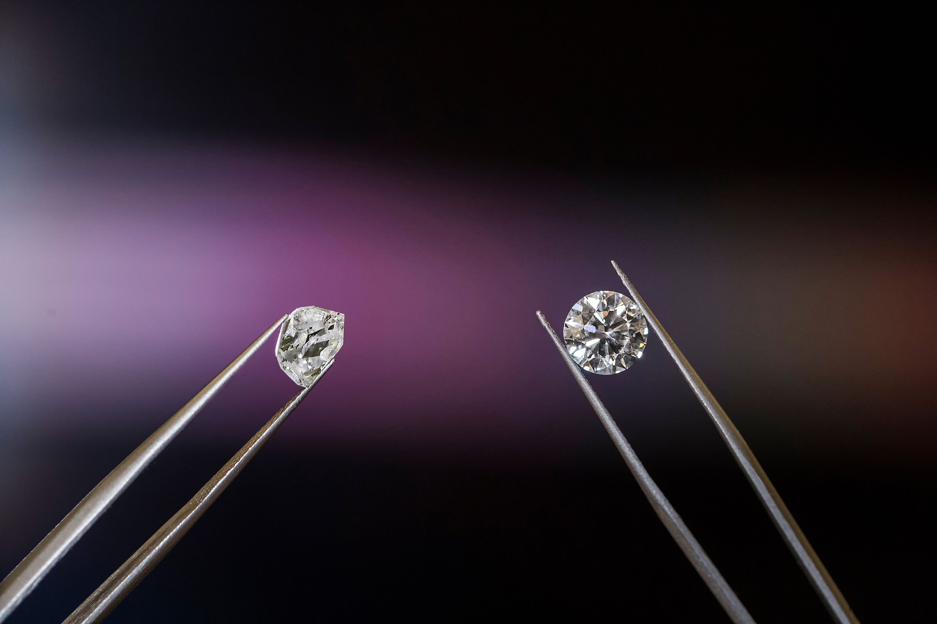 Two diamonds held by metal tweezers being compared side by side against a dark background